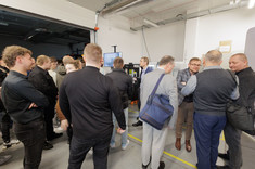 Uczestnicy szkolenia zgromadzeni wokół stanowiska obróbkowego w hali produkcyjnej, prowadzą rozmowy i obserwują prezentację 